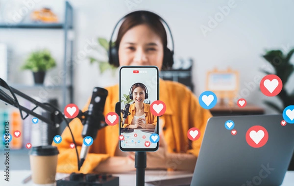 Obraz Vlogger live streaming podcast review on social media, Young Asian woman use microphones wear headphones with laptop record video. Content creator concept.