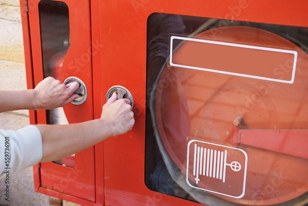 Fototapeta Close-up hands open fire cabinet with fire extinguisher and fire hoses