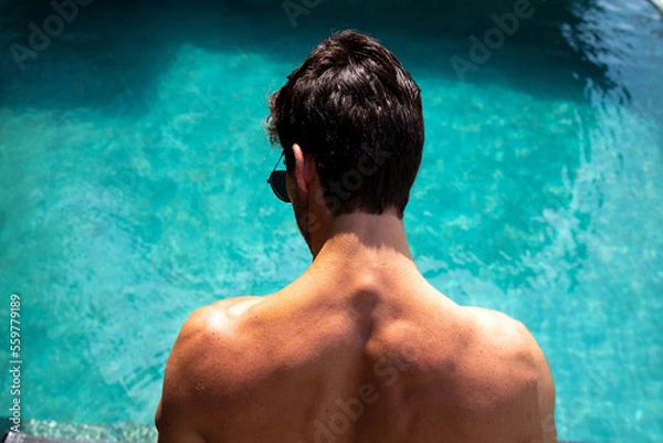 Obraz muscular man with his back to the camera looking into a blue pool, person in the pool