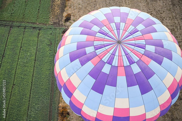 Fototapeta arial view of large pink, purple, and blue hot air balloon from the top rising over a bright green field