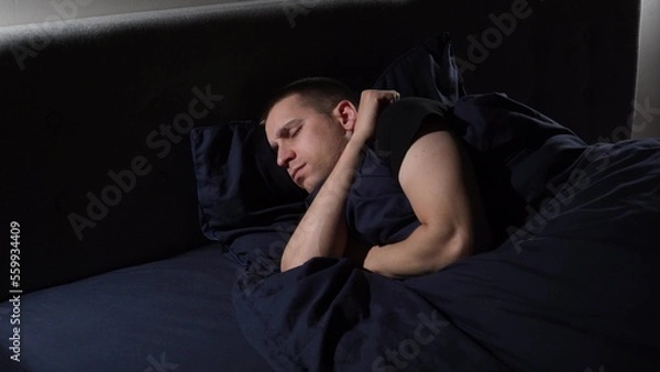 Fototapeta Disturbed sleep. I have nightmares. The young guy tosses and turns in bed.