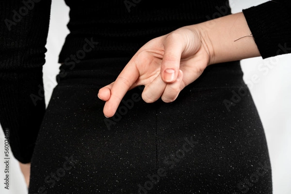 Fototapeta Close up of crossed fingers behind a woman's back in black dress