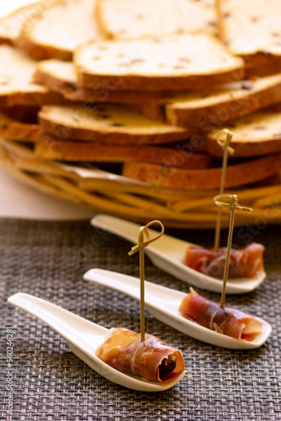 Fototapeta Jamon. Dry Spanish ham, Bellota, Italian Prosciutto Crudo or Parma ham. Slicing Spanish iberic ham served as tapas with bread slices on background. Traditional food. Canapes with cured ham...