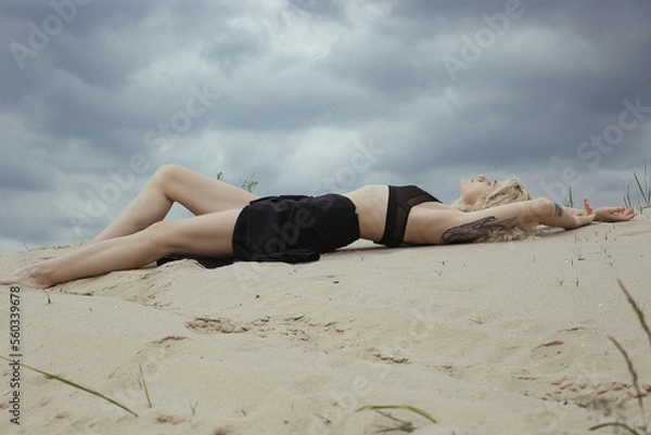 Fototapeta Sensual bare lady lying on beach scenic photography. Picture of person with overcast sky on background. High quality wallpaper. Photo concept for ads, travel blog, magazine, article