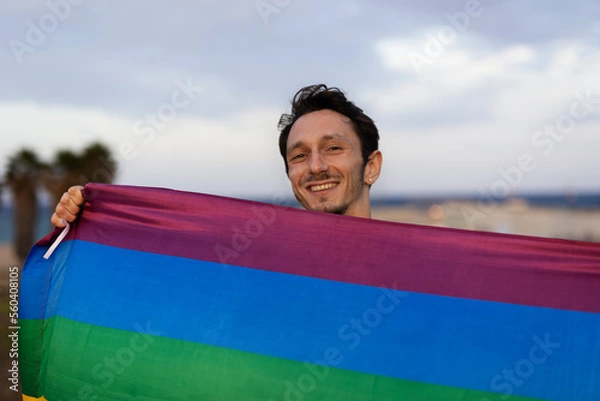 Fototapeta Happy gay man having fun holding rainbow flag symbol of LGBT community.