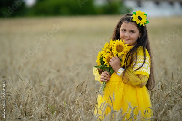 Fototapeta A girl in a wheat field with a bouquet of sunflowers.