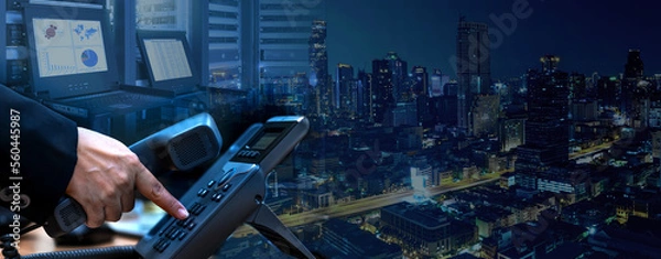 Fototapeta IP telephony management and telecommunications services system concept, business hand dialing ip telephone device, datacenter with rack servers and monitor, night cityscape background