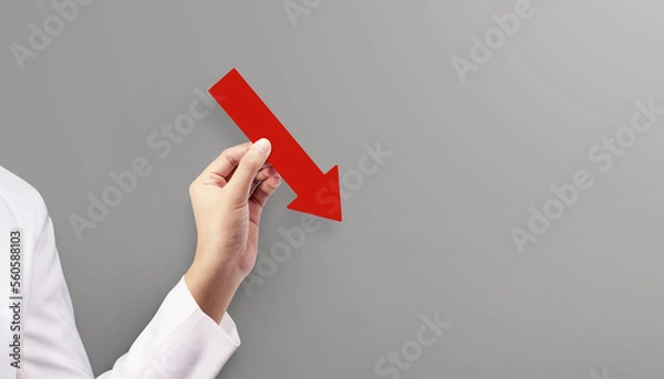 Fototapeta Woman holding red graph chart arrow that is pointing down at grey background. Concept of Global Recession.