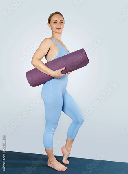Obraz A slender girl in a blue tracksuit holds a yoga mat. The instructor goes to class.