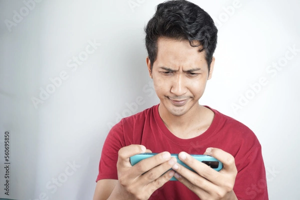 Fototapeta Photo of young man moody anxious play game mobile bite lips failure isolated over white color background