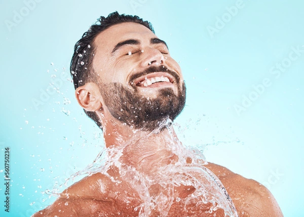 Fototapeta Water, splash and skincare with face of man for shower, self care and natural cosmetics. Luxury, hydration and refreshing with model for dermatology, wellness and cleaning in blue background studio