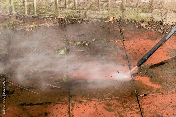 Fototapeta A power pressure washer using a pressurised water stream to clean a dirty stained patio