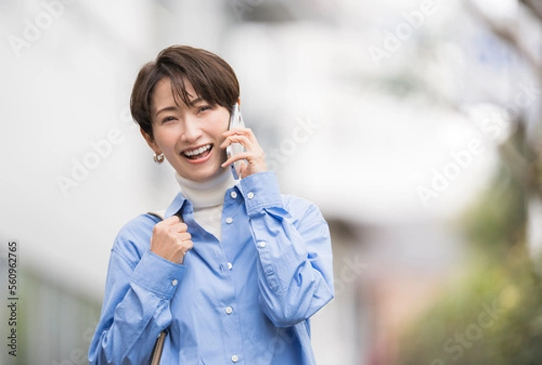Obraz 携帯電話で話ながら街を歩く笑顔のアジア人女性	