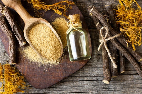 Fototapeta Glass bottle of licorice root essential oil with liquorice fiber on rustic background ( glycyrrhiza glabra )
