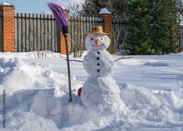 Fototapeta  Snowman in a straw hat and a broom in his hand in a snowy garden.