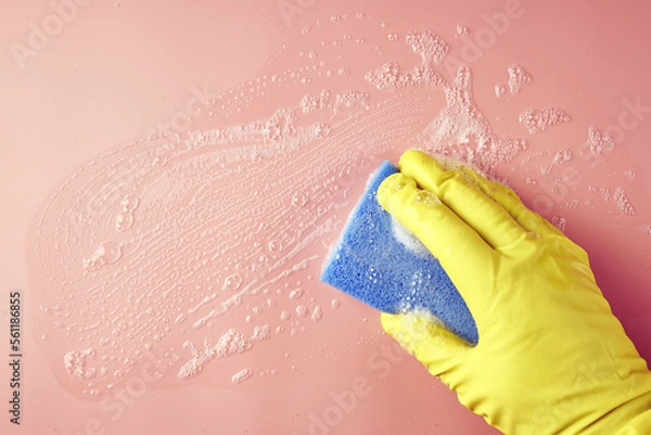 Obraz a hand in a shopping glove wipes soap suds from a pink background with a sponge
