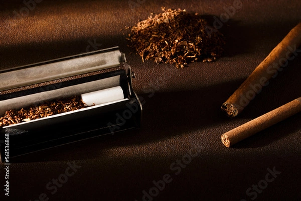Fototapeta Hand-rolled cigarette, rolling machine, cigarillos, scattered tobacco on background, cigarette roll with filter, cigarette filters.