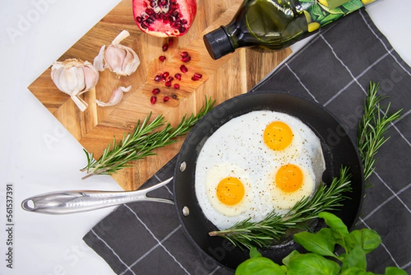 Fototapeta breakfast or brunch, fried eggs in black pans and red pomegranate with garlic and basil. view from the top.