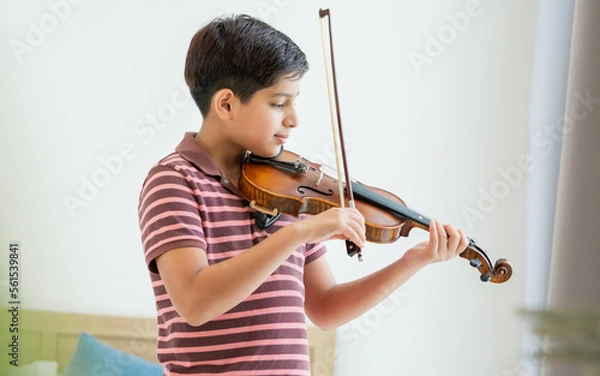 Fototapeta Indian handsome teenage boy, smiling, playing, practicing violin musical instrument with happiness in bedroom at cozy home in leisure time, smiling, having copy space. Education, Lifestyle, Concept.