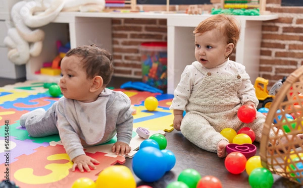 Fototapeta Two adorable babies playing with balls sitting on floor at kindergarten