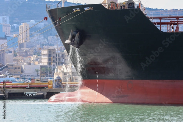 Fototapeta Large anchored cargo ship discharging ballast water out from Anchor's hub.