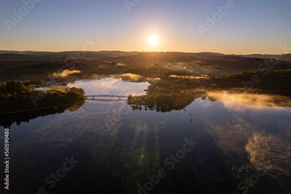 Fototapeta Aerial view of Lac de Saint Pardoux and its footbridge at sunrise in autumn with fog and mirror water