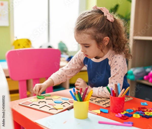 Fototapeta Adorable blonde girl playing with maths puzzle game sitting on table at kindergarten