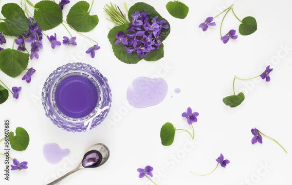 Obraz Syrup and jelly from viola odorata flowers in glass, spoon and violet fresh flower with leaves decorative arranged on white table background, shot from above. Spring herbal sweet product. Top view.