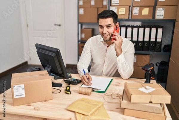 Fototapeta Young hispanic man e-commerce business worker talking on the smartphone at office