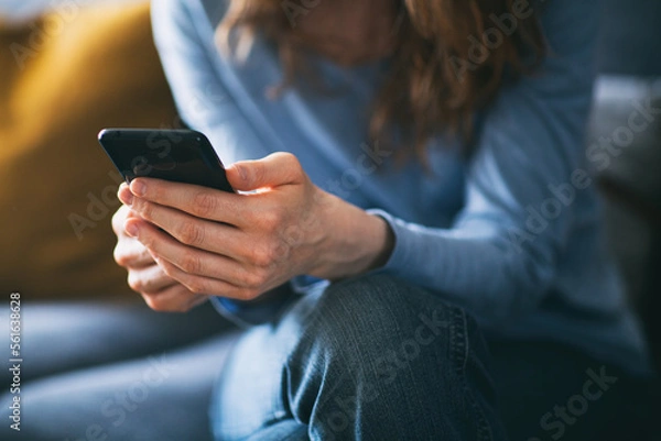 Fototapeta Young woman using a mobile phone on the couch at home