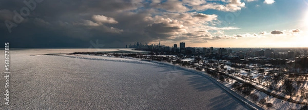 Obraz Aerial panorama of the Lake Michigan shoreline on the north side of Chicago covered in frozen ice 'pancakes' as clouds move past the downtown skyline in the distance and the sun begins to set.