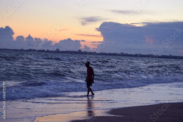 Fototapeta The silhouette on a beach. There is a man walks on the beach of Black sea. There is a town in the background. Sunset.