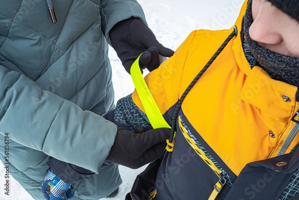 Obraz Caring mother puts a reflective tape on her child's hand. Fluorescent signal stripes for pedestrian visibility in the car's headlights at dark time.