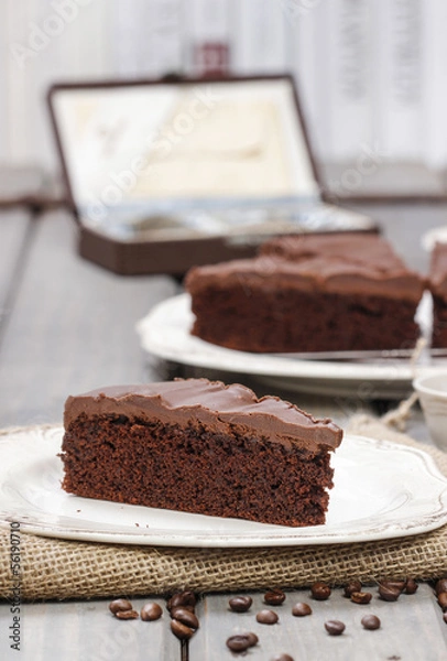 Fototapeta Chocolate cake on white plate, on hessian. Coffee beans on wood
