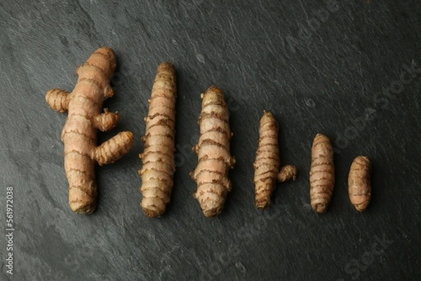 Fototapeta Many raw turmeric roots on black textured table, flat lay