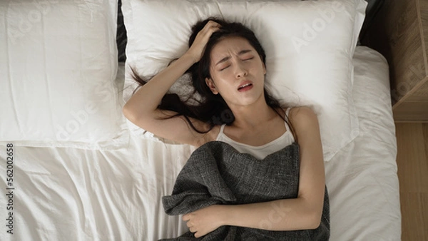 Obraz above view of a restless asian japanese woman turning and tossing in agony on bed while haunted with nightmare during her sleep in the bedroom at home