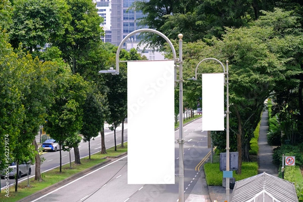Fototapeta Tall vertical hanging blank advertising banners posters mockup; lush plants and tress in background; for OOH out of home lamp post media.