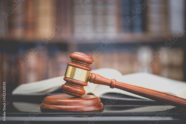 Fototapeta Legal office of lawyers, justice and law concept : Judge's gavel or hammer and base used by a judge person on a desk in a courtroom with blurred books and a bookshelf or bookcase in the background.