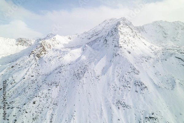 Fototapeta Snow covered peaks of mountains during winter on a sunny day with clouds in Fluela Pass, Davos, Switzerland.
