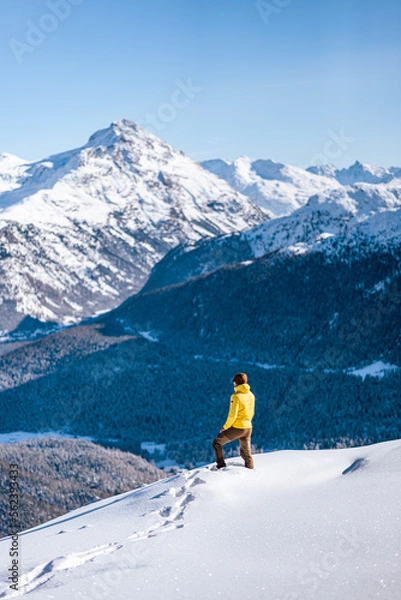 Fototapeta Caucasian man standing on top of a hill looking at winter snow mountain landscape and forests on a sunny day around St. Moritz, Switzerland.