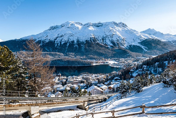 Fototapeta Top view of the lake and town of St. Moritz covered in snow during winter on a sunny day in Switzerland.