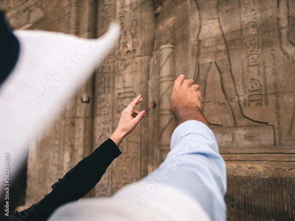 Fototapeta Hands of white caucasian man and woman pointing at Egyptian hieroglyphs on a wall.
