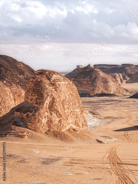 Fototapeta The view of car tracks and rocks in the sand of Valley of Agabat, White Desert, Egypt.