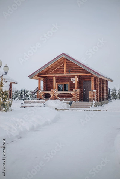 Fototapeta A wooden house in a snowy forest around Christmas trees