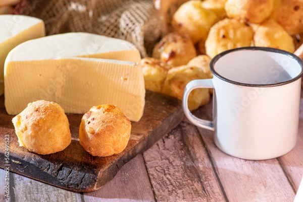Fototapeta Cheese bread and more, cheese bread, manioc flour cookies and Minas cheese arranged on a rustic wooden surface with accessories, selective focus.