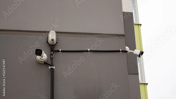 Fototapeta Surveillance cameras on the wall of a high-rise apartment building. Video equipment for security system control of the area on the street.