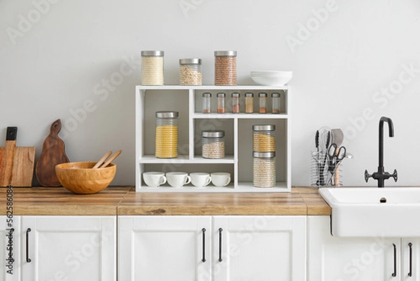 Fototapeta Jars with cereals, spices and utensils on kitchen counter