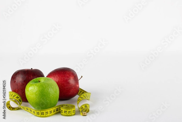 Fototapeta Red and green apples in rolled up on a measuring tape, symbolizing healthy life, on white background