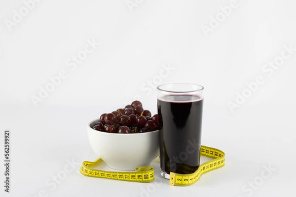 Fototapeta Glass of grape juice accompanied by a bowl of fresh and cold grapes on white background