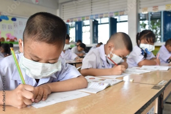Fototapeta Elementary school students wearing hygienic mask while studying in the classroom.